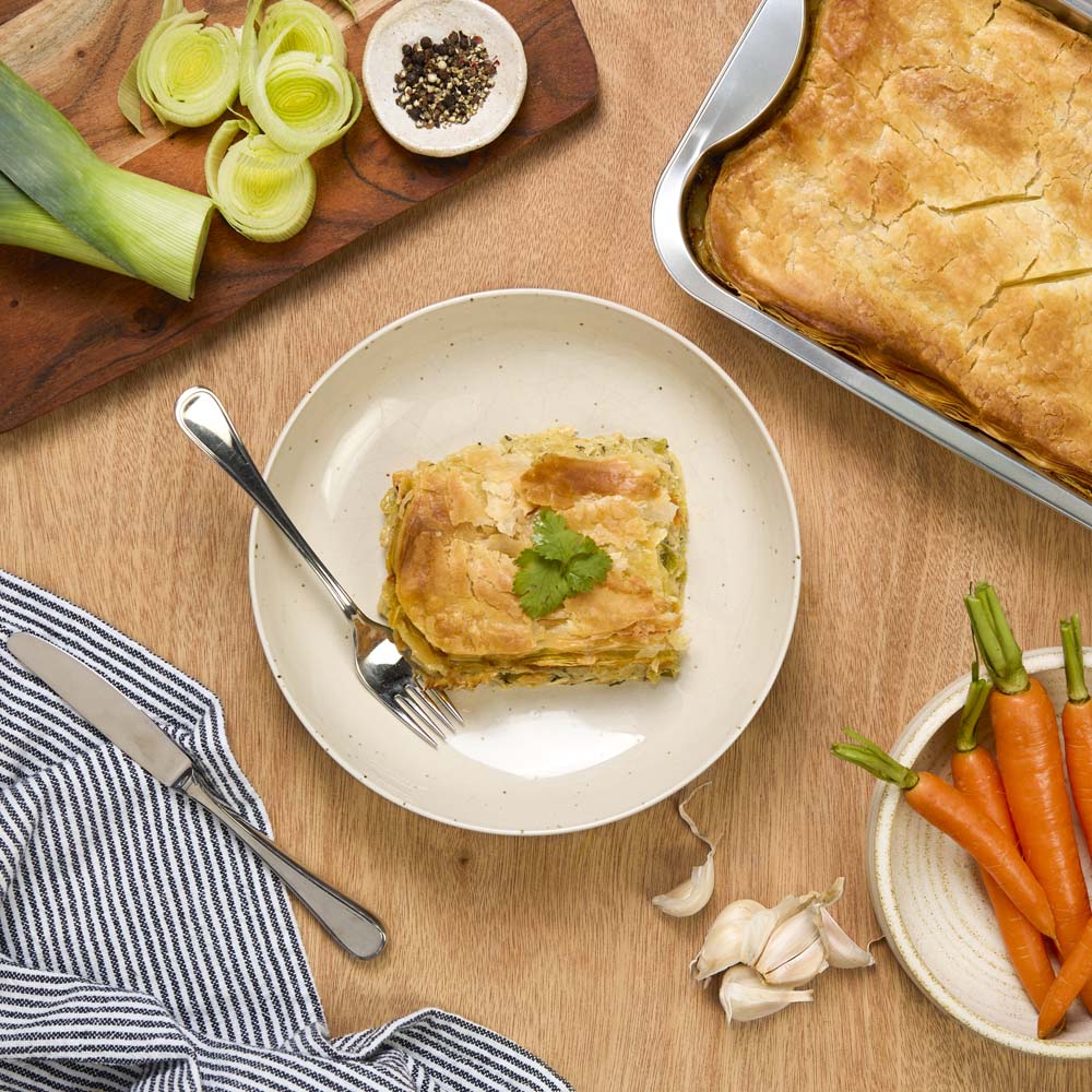 Country Chicken, Leek & Tarragon Pie pie on a plate with carrots and leeks on a wooden table