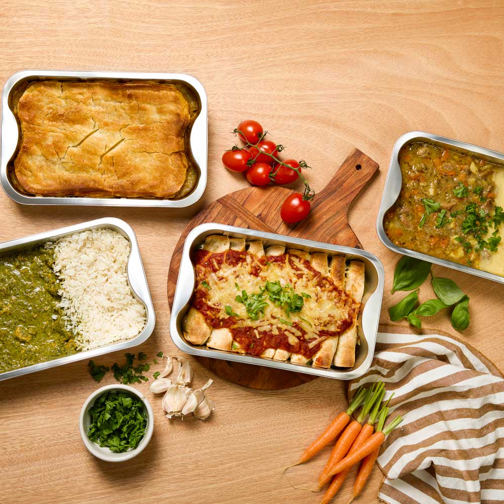 Assorted ready-made meals on a wooden table with vegetables and a striped cloth.