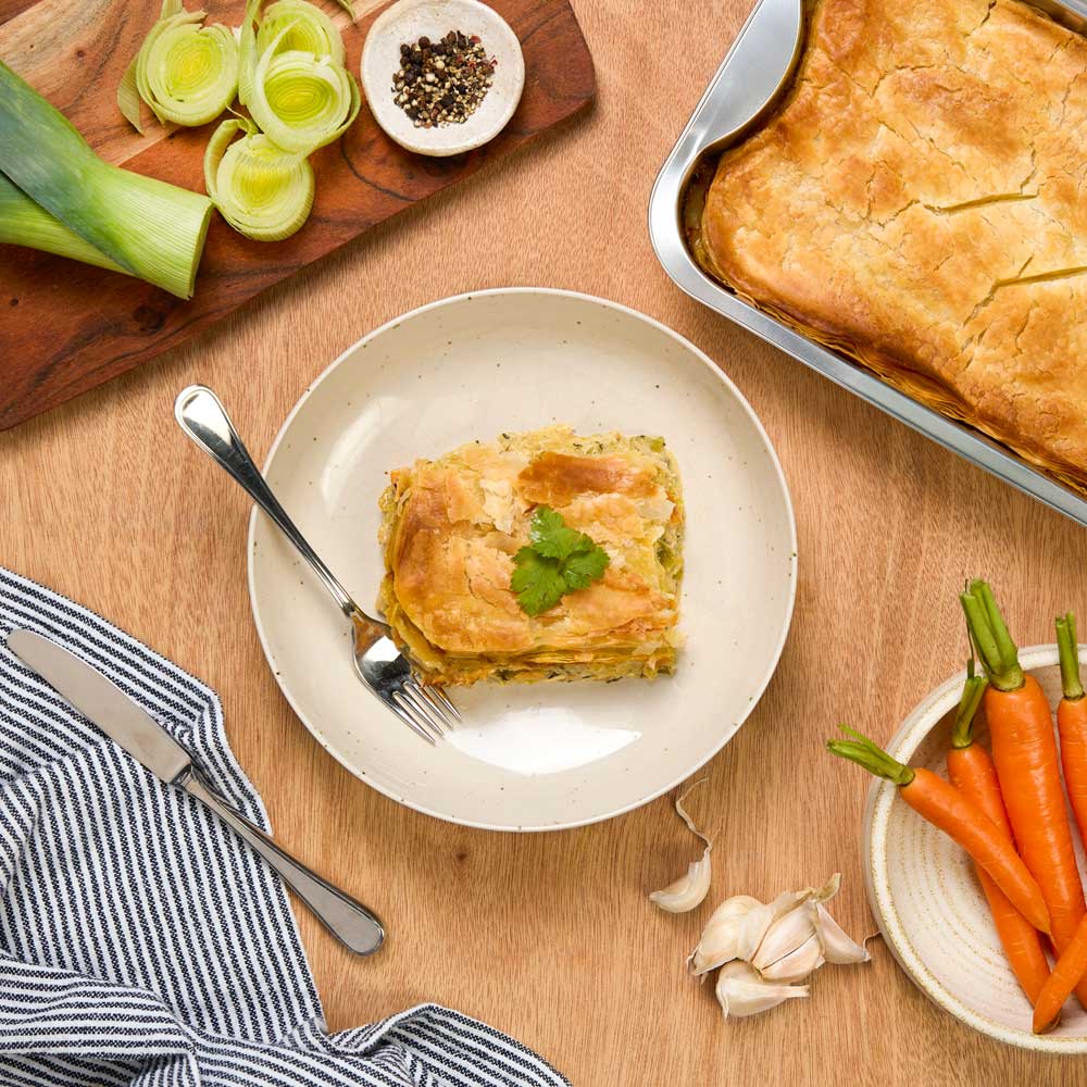 Assorted ready-made meals on a wooden table with vegetables and a striped cloth. Displayed on home page.